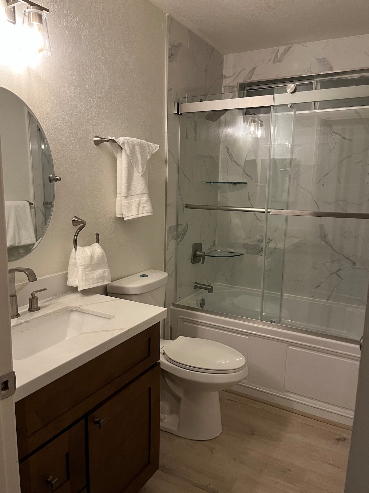 Renovated main bath with glass shower door, vanity, and marble surround